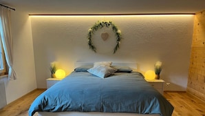 A bedroom with a bed, two bedside lamps, a wall-mounted heart decoration, and a window with curtains. - Flott Appartement/Fewo, Dusche und Bad, WC, 1 Schlafraum 2.5-Zimmerwohnung by Interhome (Adelboden)