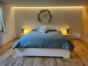 Ein Schlafzimmer mit einem Bett, zwei Nachttischlampen, einer Wanddekoration im Herzform und einem Fenster mit Vorhängen.