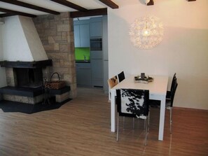 A dining area with a stone fireplace, a modern chandelier, and a view into a kitchen. - Helios Appartement/Fewo, Dusche, WC, 3 Schlafräume 4-Zimmerwohnung by Interhome (Adelboden)