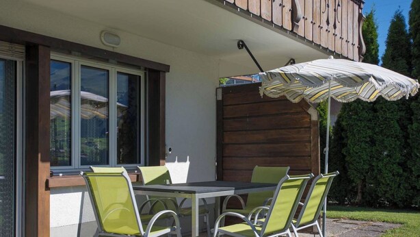 An outdoor patio with a table and chairs, a wooden fence, and a large umbrella. - Helios Appartement/Fewo, Dusche, WC, 3 Schlafräume 4-Zimmerwohnung by Interhome (Adelboden)
