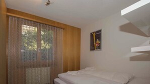A bedroom with a bed, a window with lace curtains, and a poster on the wall. - Helios Appartement/Fewo, Dusche, WC, 3 Schlafräume 4-Zimmerwohnung by Interhome (Adelboden)