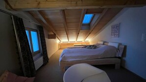 Un dormitorio con techo inclinado, dos camas, una bañera y un ventanal.