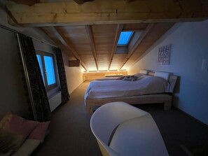 Ein Schlafzimmer mit schrägem Dach, zwei Betten, einer Badewanne und einem Fenster.