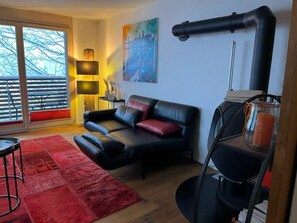 Ein modernes Wohnzimmer mit einem schwarzen Ledersofa, einem roten Teppich, einem Gemälde und einer schwarzen Pfeilerkonstruktion.