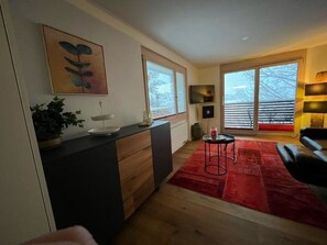 A modern living room with a red rug, a black sofa, a small round table, and a painting on the wall. - Chalet Abrigo Appartement/Fewo, Bad, WC, 1 Schlafraum by Interhome (Adelboden)