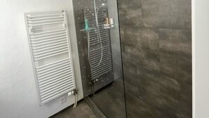 Un baño moderno con cabina de ducha de vidrio, radiador de pared y suelo de baldosas.