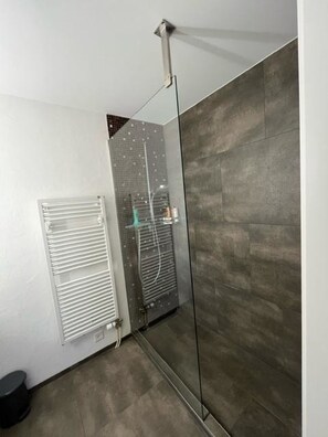 Ein modernes Badezimmer mit Duschkabine aus Glas, Wandradiator und gefliestem Boden.