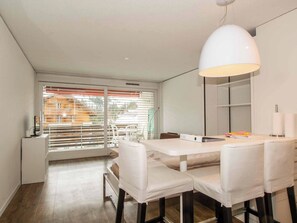 A modern dining area with a white table and chairs, a pendant light, and a view through large windows. - Studio Selva Appartement/Fewo, Dusche, WC, 1 Schlafraum 1-Zimmerwohnung by Interhome (Adelboden)