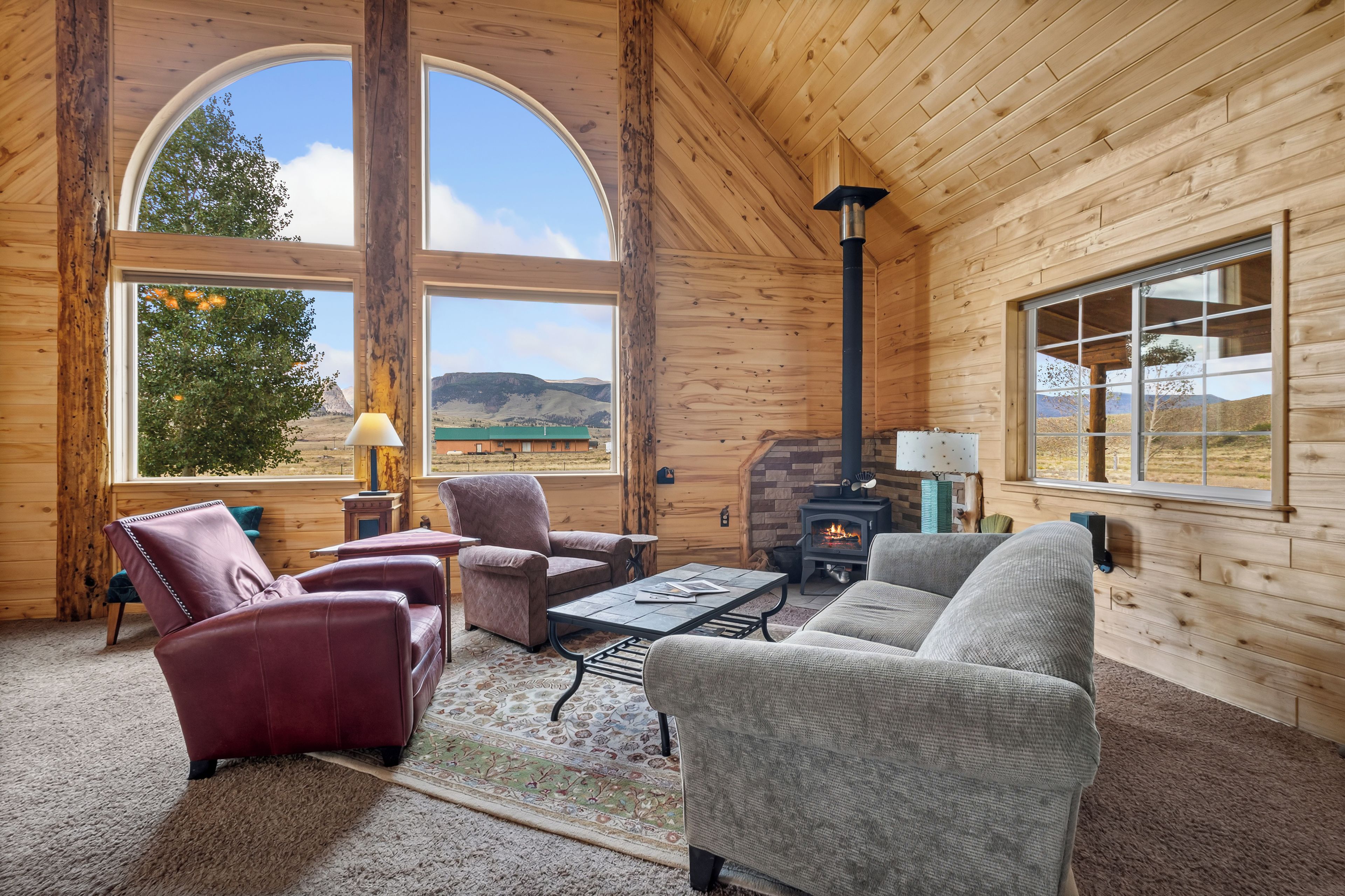 A log cabin interior with a fireplace, large windows, and a cozy seating area.