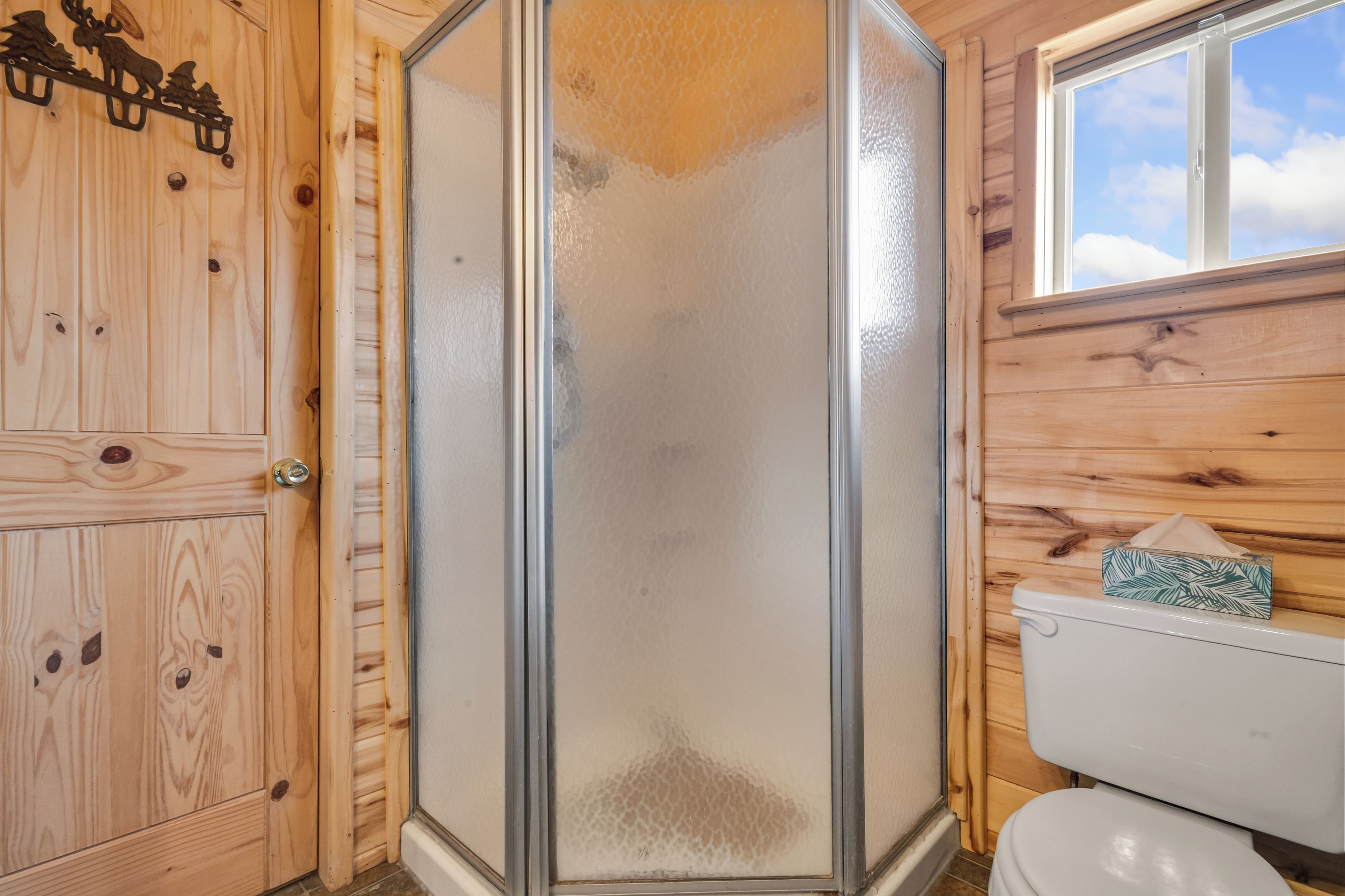 Ein Badezimmer einer Holzhütte mit einer Duschkabine aus Glas, einer Toilette und einem Fenster.