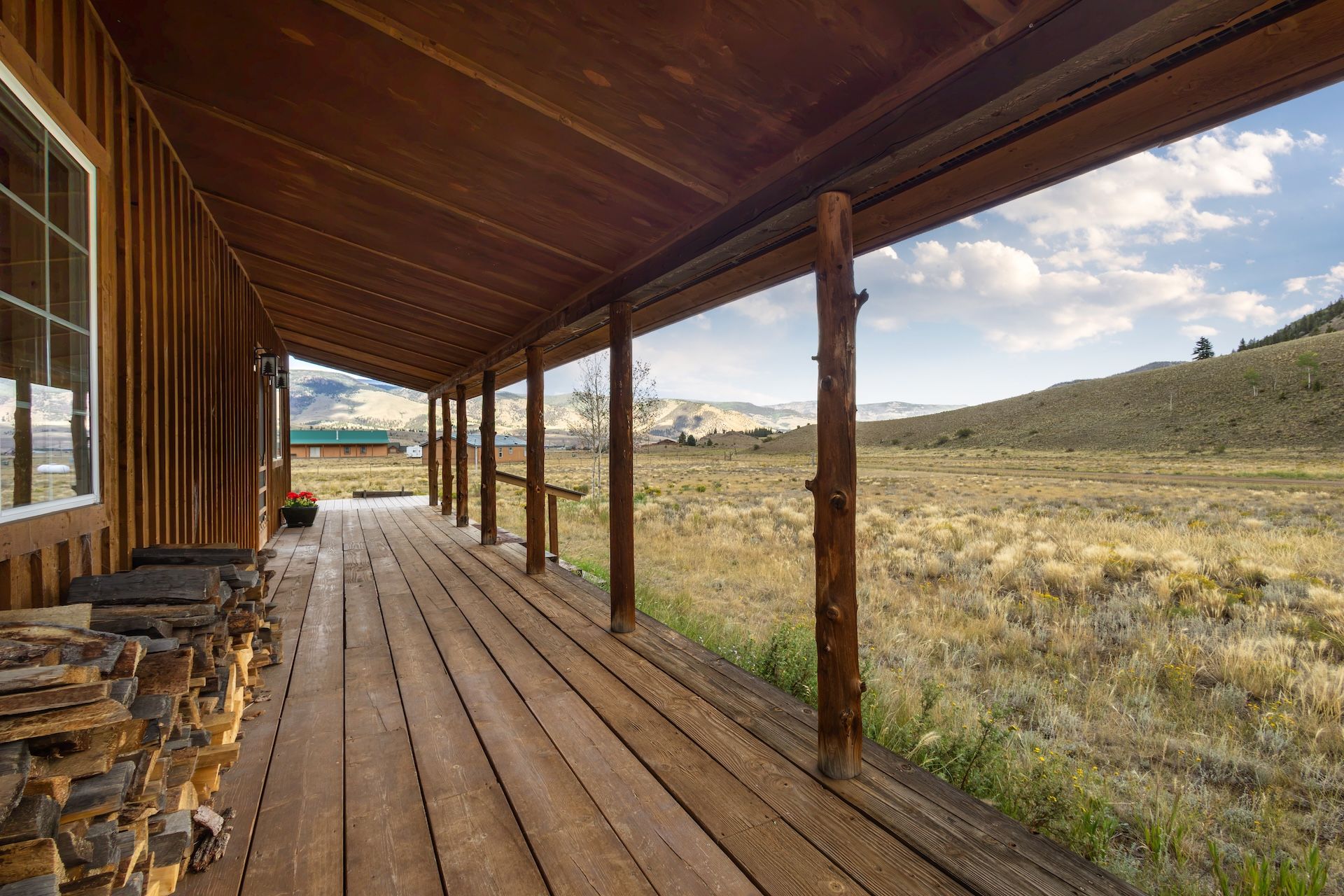 A wooden porch with a view of a grassy field and mountains.