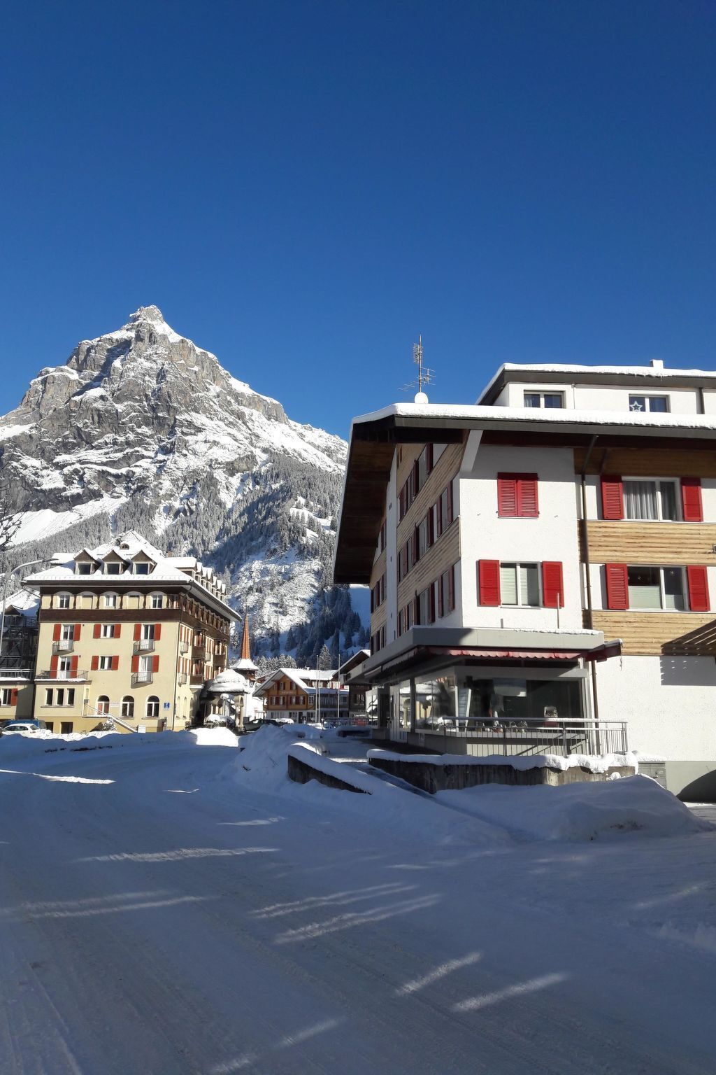 A snow-covered mountain with a building featuring balconies and red shutters.