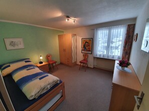 A bedroom with a bed, a desk, a chair, a wardrobe, a window with curtains, and a wall with a framed picture. - Blüemlisalpblick Appartement/Fewo, Dusche und Badewanne, Balkon 6-Bett Wohnung by Interhome (Kandersteg)