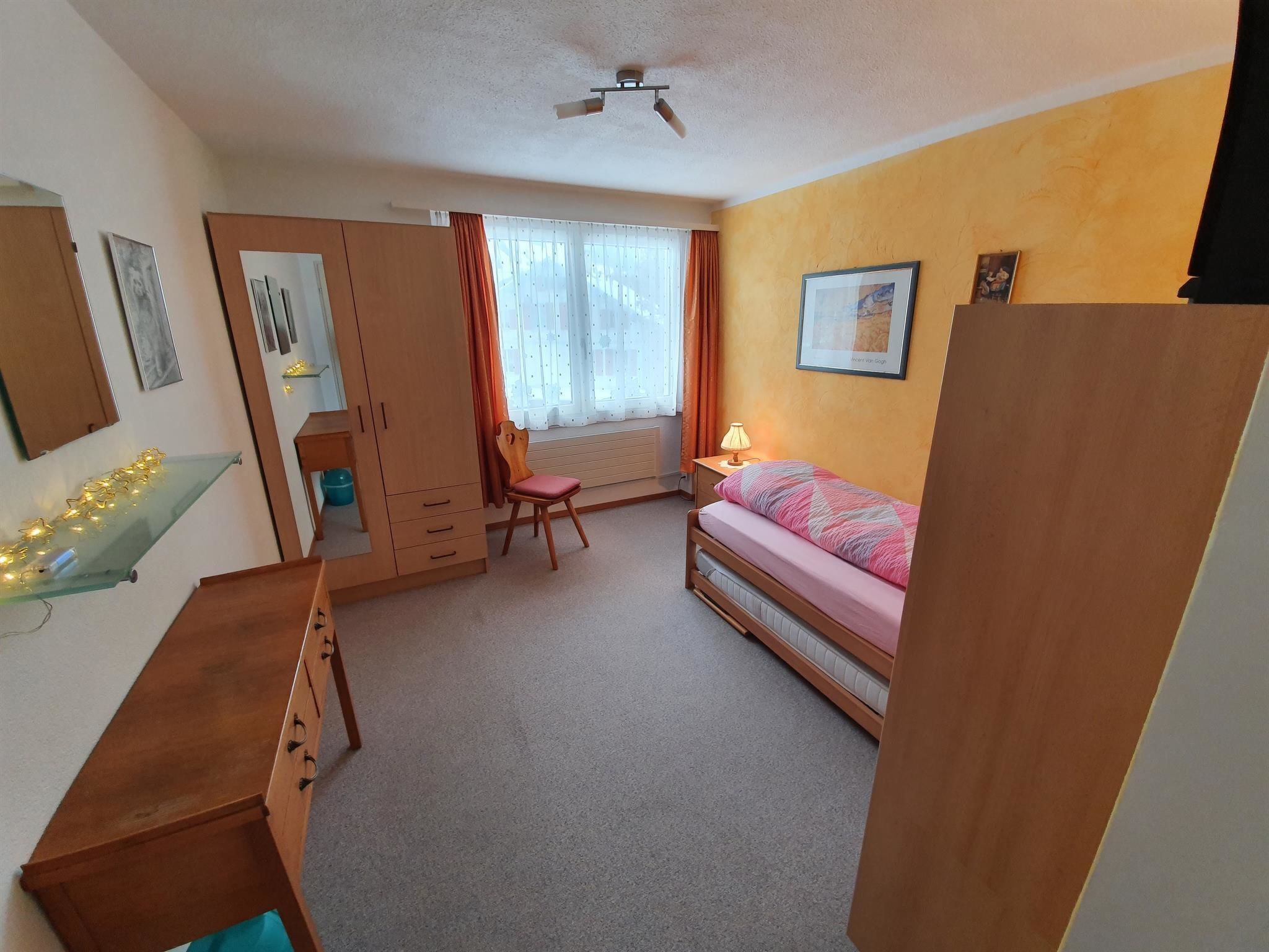 Une chambre à coucher comprenant un lit, un bureau, une chaise, une armoire et une fenêtre avec des rideaux.