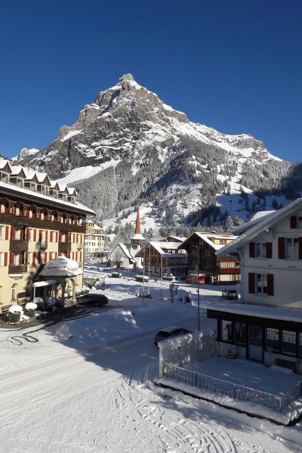 A snow-covered town with traditional buildings, a mountain in the background, and a clear sky.