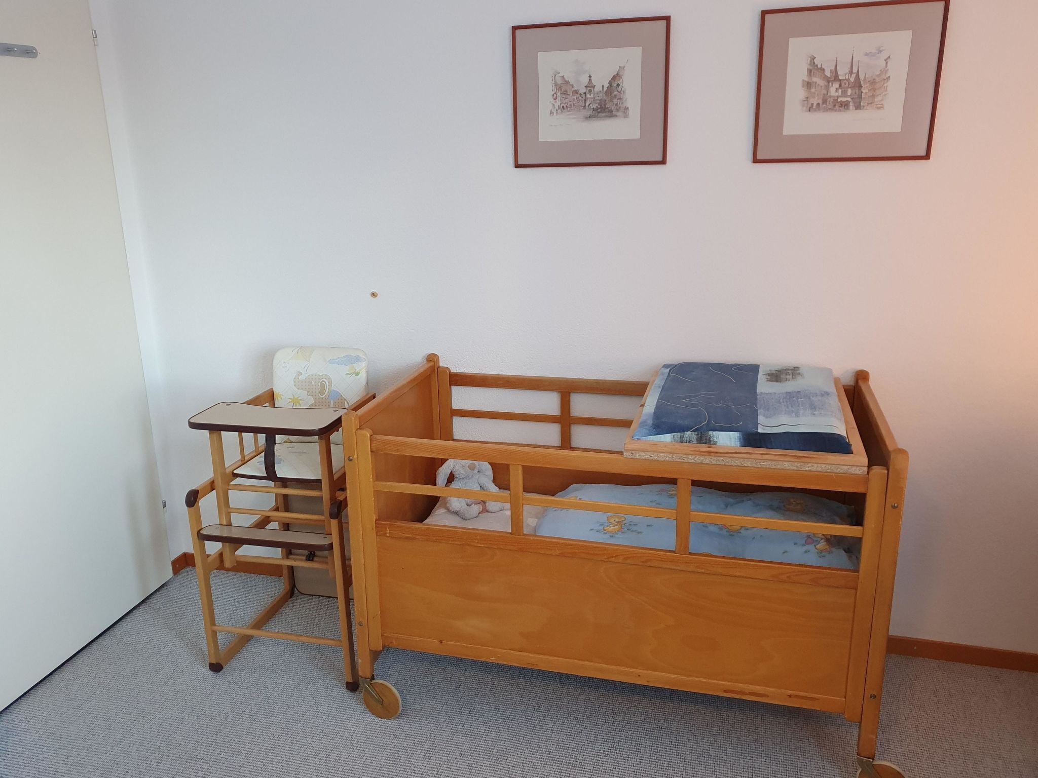 Ein Kinderzimmer mit einem hölzernen Etagenbett, einem Schreibtisch und Stuhl, einem kleinen Tisch mit Kissen sowie zwei gerahmten Bildern an der Wand.