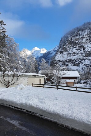 A snowy landscape with a mountain in the background, a wooden fence, and a building with a snow-covered roof. - Blüemlisalpblick Appartement/Fewo, Dusche und Badewanne, Balkon 6-Bett Wohnung by Interhome (Kandersteg)