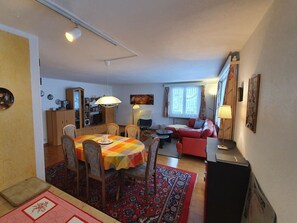 A living room with a red sofa, a dining table with chairs, and a kitchen area with cabinets and a television. - Blüemlisalpblick Appartement/Fewo, Dusche und Badewanne, Balkon 6-Bett Wohnung by Interhome (Kandersteg)