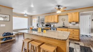 A modern kitchen with wooden cabinets, a central island with stools, a ceiling fan, and a view of the living area.