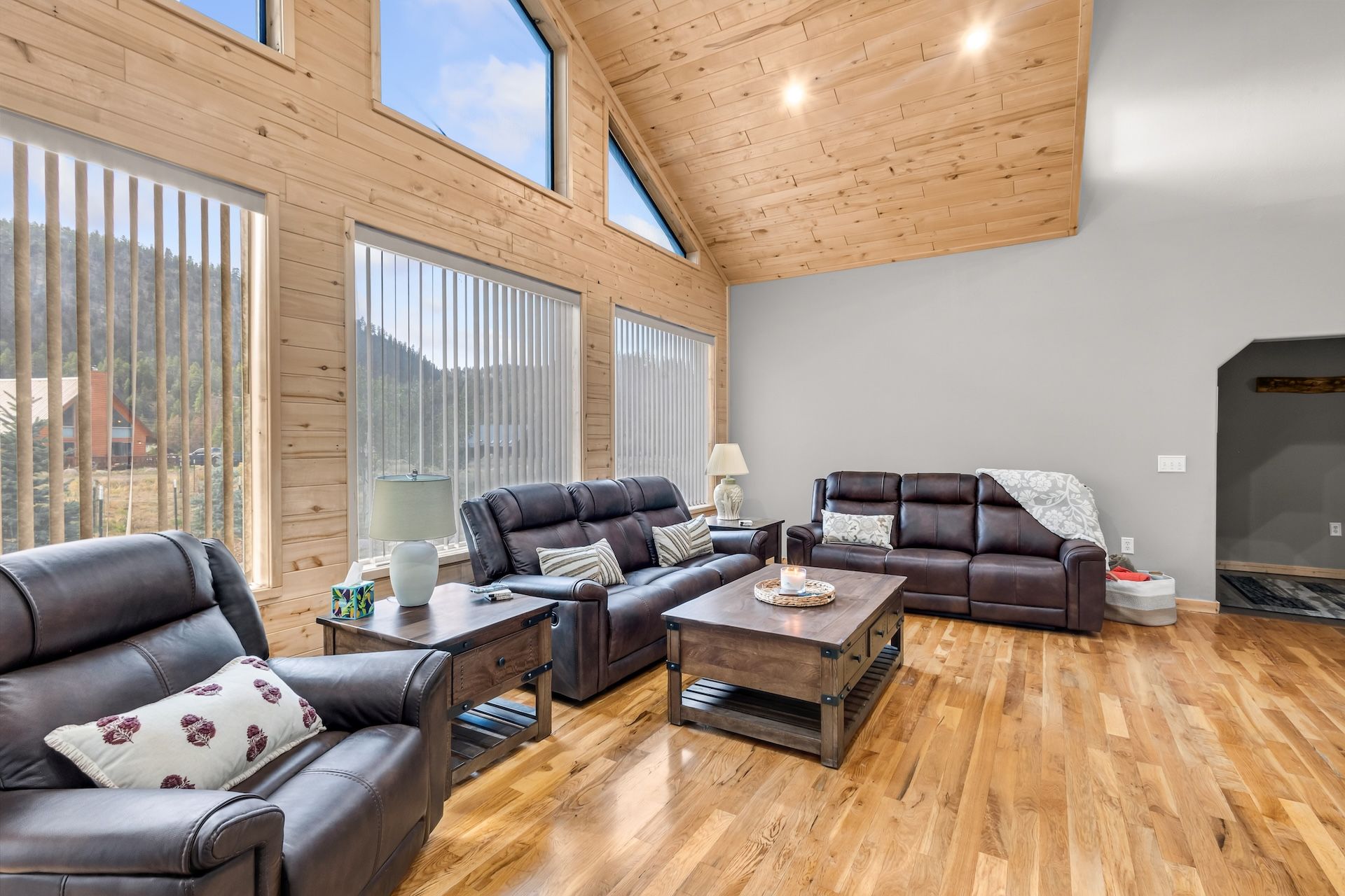 A spacious living room with a high ceiling, wooden walls, and large windows.