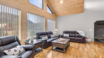 A spacious living room with a high ceiling, wooden walls, and large windows.