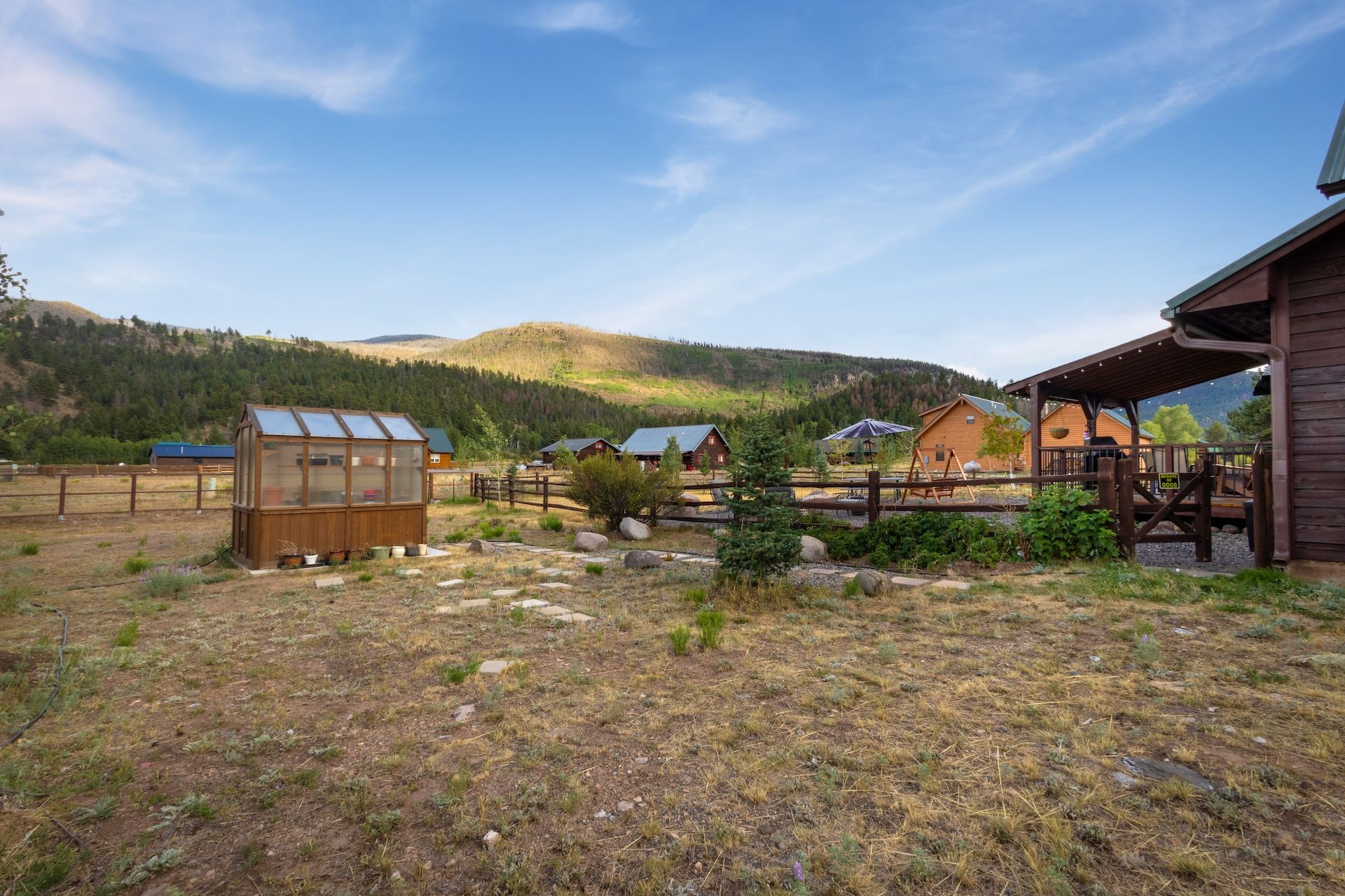 A rustic cabin with a wooden deck and a glass greenhouse.