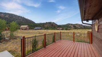 A wooden deck with a metal railing overlooking a rural landscape with houses and mountains.