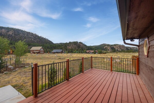 A wooden deck with a metal railing overlooking a rural landscape with houses and mountains.