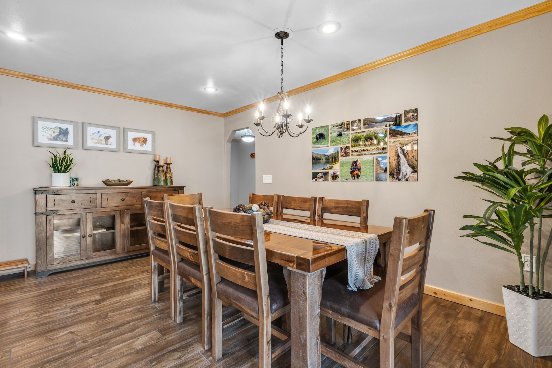 A dining area with a wooden table and chairs, a chandelier, and a wall with framed pictures.