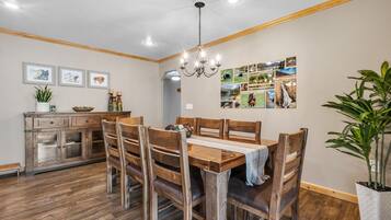 A dining area with a wooden table and chairs, a chandelier, and a wall with framed pictures.