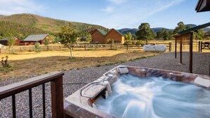 Ein Whirlpool mit einer Holzterrasse in ländlicher Umgebung, im Hintergrund Häuser und Berge.