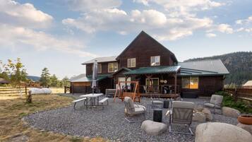 A rustic wooden building with a sloped roof, outdoor seating area with tables and chairs, and a gravel ground.