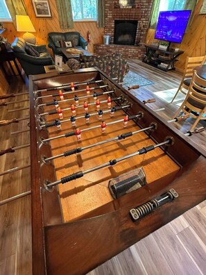 A foosball table in a room with a fireplace, a television, and a cozy seating area. - Unique Big Bear Experience, Family Game Room, plenty of space to lounge - BEST location to everything! Hot tub and huge yard, great for sledding. So close to downtown - walk to The Village for boutique shopping! (Big Bear Lake)