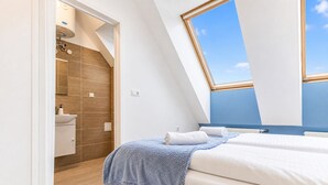 A bedroom with a skylight, a bathroom with a shower, and a bed with a blue blanket.