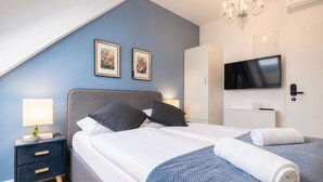 A bedroom with a bed, bedside tables, a TV, and a chandelier.