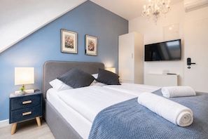A bedroom with a bed, bedside tables, a TV, and a chandelier.