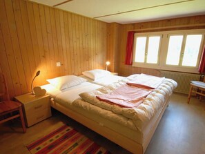 A bedroom with a double bed, a bedside table with a lamp, a chair, and a window with curtains. - Stockbrunä Appartement/Fewo, Bad, WC, 2 Schlafräume by Interhome (Adelboden)