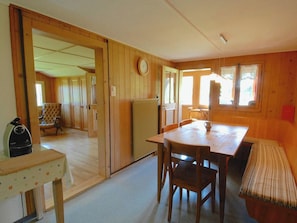 A cozy room with a wooden floor, a dining table with chairs, a radiator, a clock on the wall, and a window with curtains. - Stockbrunä Appartement/Fewo, Bad, WC, 2 Schlafräume by Interhome (Adelboden)