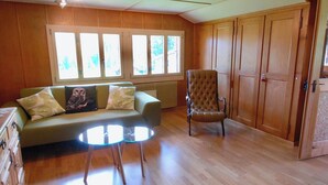 A room with a wooden floor, a green sofa with cushions, a round glass table, a brown armchair, and a large window with multiple panes. - Stockbrunä Appartement/Fewo, Bad, WC, 2 Schlafräume by Interhome (Adelboden)