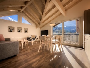 A spacious living area with a high ceiling, wooden beams, a sofa, a dining table, chairs, and artwork on the walls. - Ferienwohnung Bunder (DG) Appartement/Fewo, Bad, WC, 3 Schlafräume by Interhome (Adelboden)