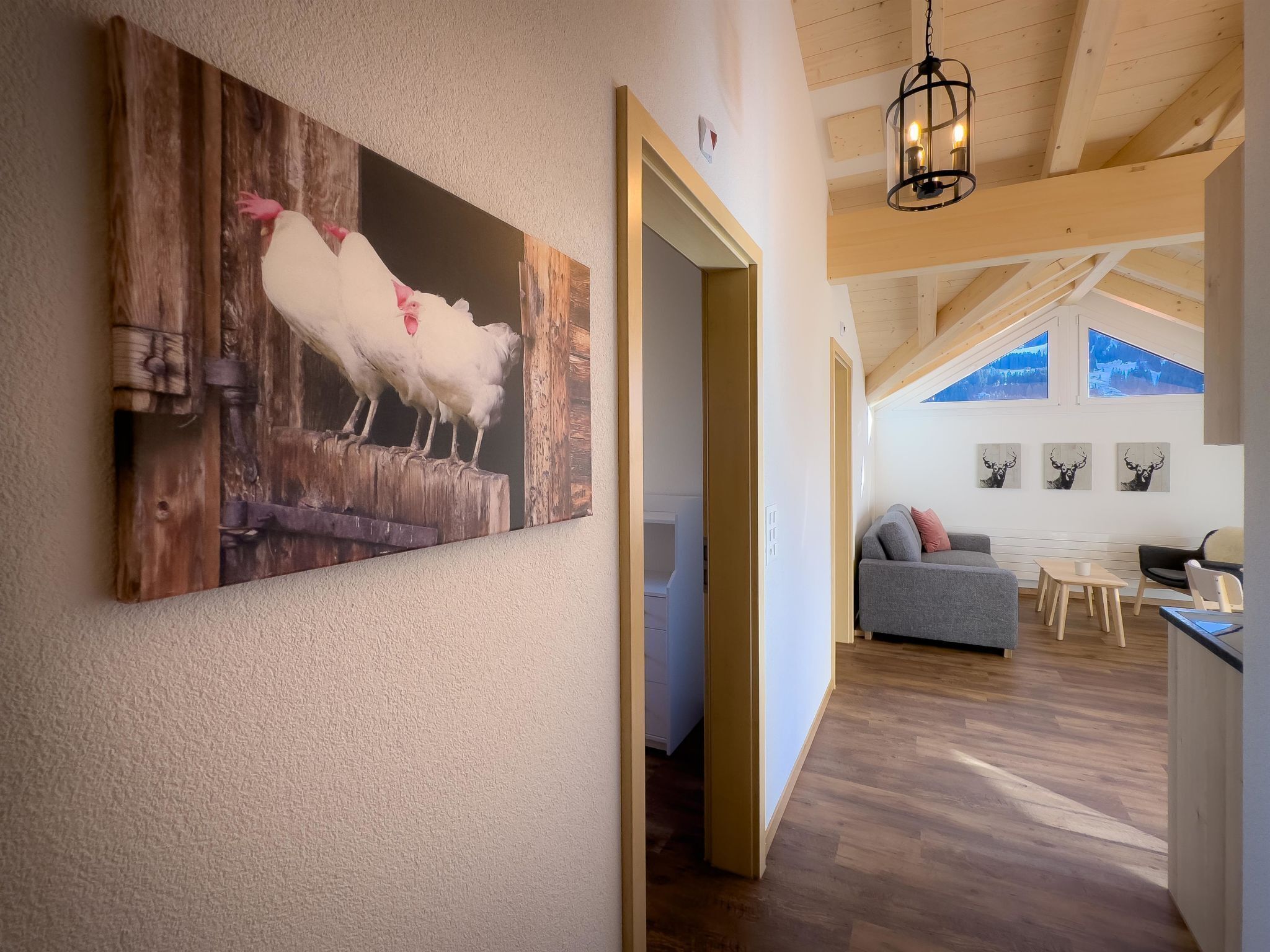 Ein Flur mit rustikaler Holzvertäfelung und einem Bild von einem weißen Schaf. Eine gemütliche Sitzecke mit grauem Sofa und einem Tisch, sowie eine Holzbalkendecke mit einer Pendelleuchte.