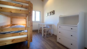 Uma cama de beliche com escrivaninha e gavetas, uma janela e um radiador.