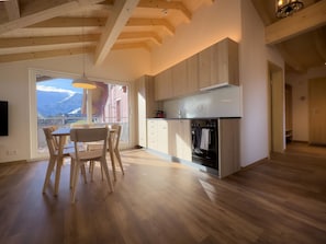 A modern kitchen with wooden cabinets, a dining area with a table and chairs, and a view of mountains through a large window. - Ferienwohnung Bunder (DG) Appartement/Fewo, Bad, WC, 3 Schlafräume by Interhome (Adelboden)