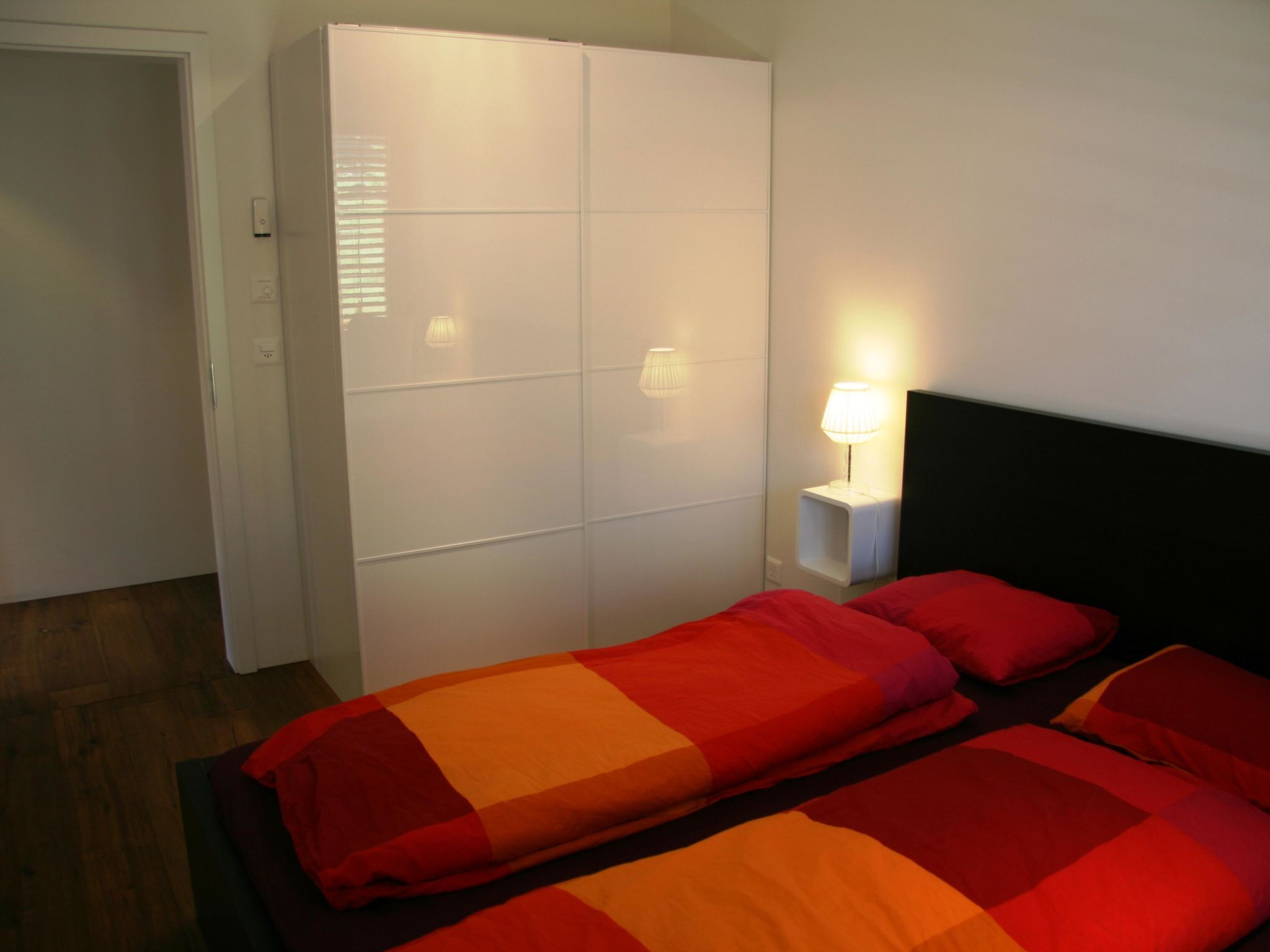Un dormitorio con una cama, un armario y una mesita de noche con una lámpara.
