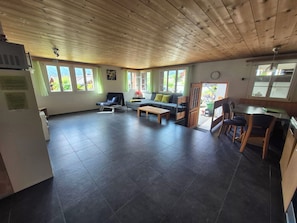 A spacious living area with a sofa, a dining table, and chairs, a kitchenette, and large windows with curtains. - Chalet Sunnegg Appartement/Fewo, Dusche, WC, 2 Schlafräume 3-Zimmerwohnung by Interhome (Adelboden)