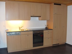 A kitchen with wooden cabinets, a dishwasher, an oven, and a sink. - Chalet Sunnegg Appartement/Fewo, Dusche, WC, 2 Schlafräume 3-Zimmerwohnung by Interhome (Adelboden)