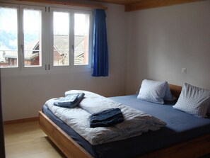 A bedroom with a bed, pillows, a window with curtains, and a view of buildings outside. - Chalet Sunnegg Appartement/Fewo, Dusche, WC, 2 Schlafräume 3-Zimmerwohnung by Interhome (Adelboden)