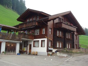 A multi-story wooden building with balconies, a garage, and a paved driveway. - Chalet Sunnegg Appartement/Fewo, Dusche, WC, 2 Schlafräume 3-Zimmerwohnung by Interhome (Adelboden)