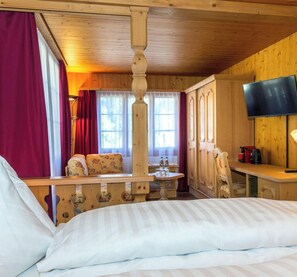 Ein Hotelzimmer mit einem Bett, einem Holztisch, einem Fernseher und einem Fenster mit Vorhängen.