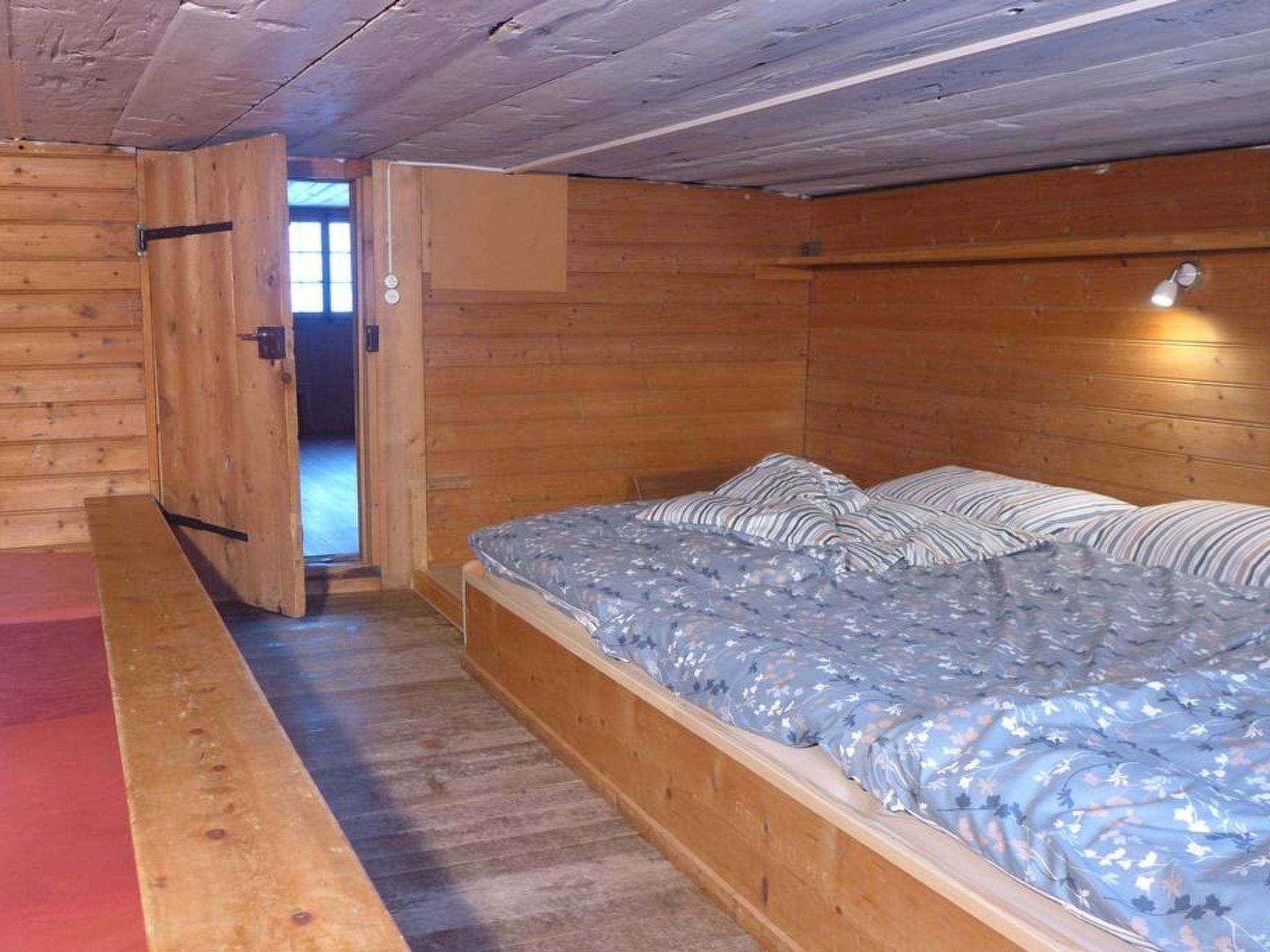 A wooden room with a bed, a door, and a window.